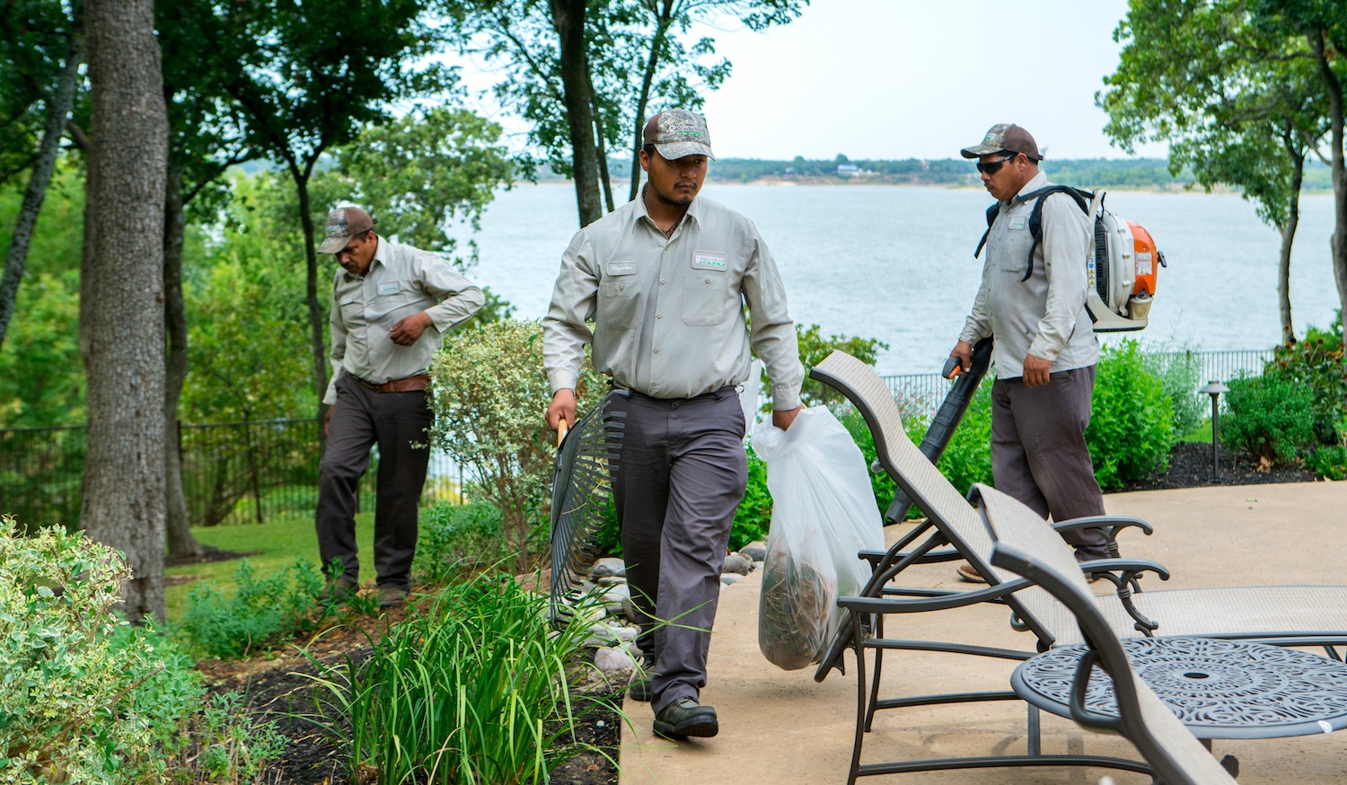 Landscape crew working together along a lakeside patio, raking, bagging debris, and using a leaf blower